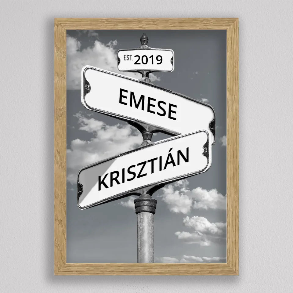 Utcanévtábla kép évszámmal tölgyfa hatású keretben, fehér táblák egy oszlopon, mögöttük felhős, szürke égbolt